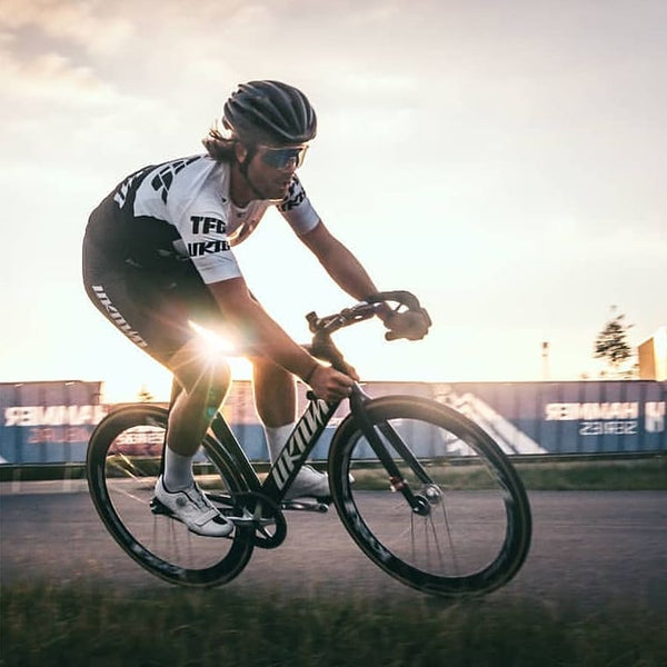 Rijder van het TFGS Unknown Racing Team in teamtenue op een Unknown fixed gear baanfiets bij zonsondergang
